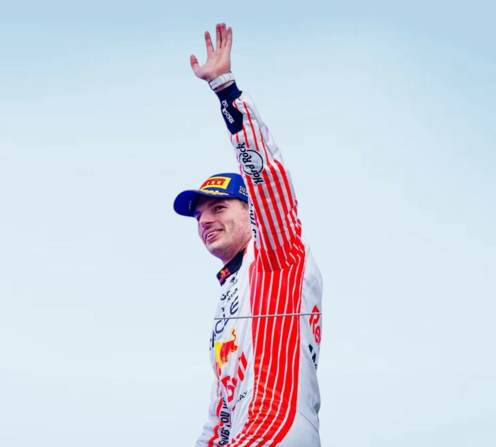 A person in a Red Bull racing suit and cap waves with one hand raised against a pale blue sky. The suit is white with bold red vertical stripes and visible Red Bull, Castrol, and other sponsor logos.