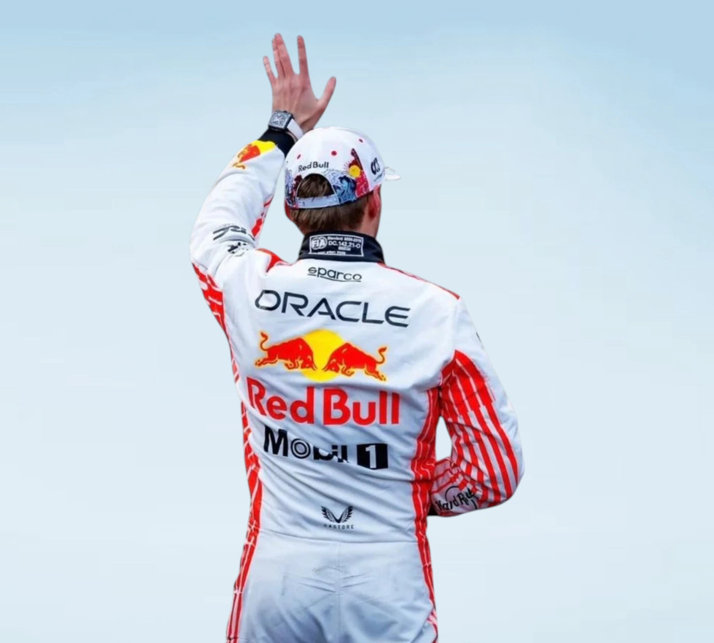 A Red Bull Racing driver seen from behind, wearing a white racing suit with red stripes and sponsor logos, including Oracle, Red Bull, Mobil 1, and Sparco, while waving with one hand against a pale sky.