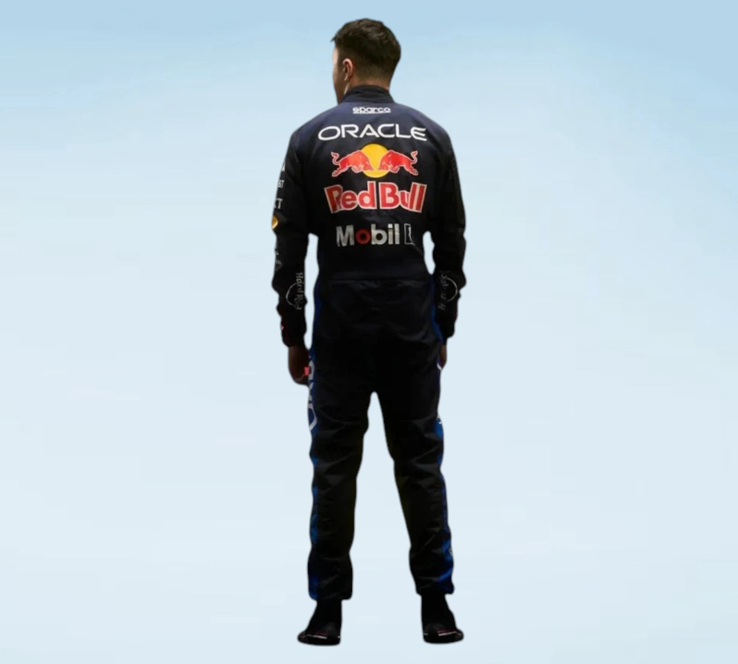 A man viewed from behind wearing a dark Oracle Red Bull Racing team jumpsuit with prominent sponsor logos including Oracle, Red Bull, Mobil 1, and Scuderia on the back, set against a light blue gradient background.