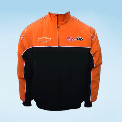 A two-tone orange and black zip-up jacket featuring a Chevrolet bowtie logo on the right chest and a pink and black checkered racing flag logo on the left chest, set against a light blue gradient background.