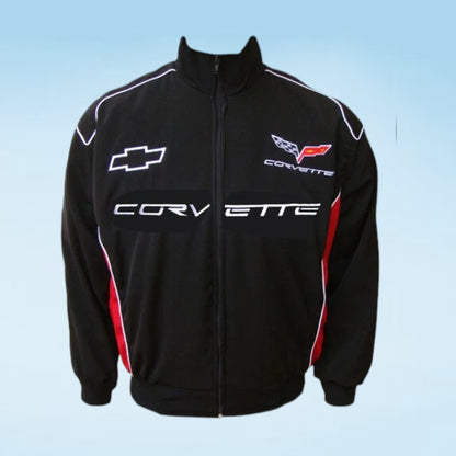 A black zip-up track jacket featuring Corvette branding, including the Chevrolet bowtie logo on the left chest and the Corvette wing emblem on the right chest, with 'CORVETTE' printed across the front. The jacket has white piping details and red side accents, set against a light blue gradient background.