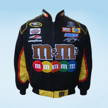 A black zip-up racing jacket featuring the large 'm&m's' logo across the front, with additional sponsor logos including Toyota, NRG, and Goodyear, and yellow and red side panels.