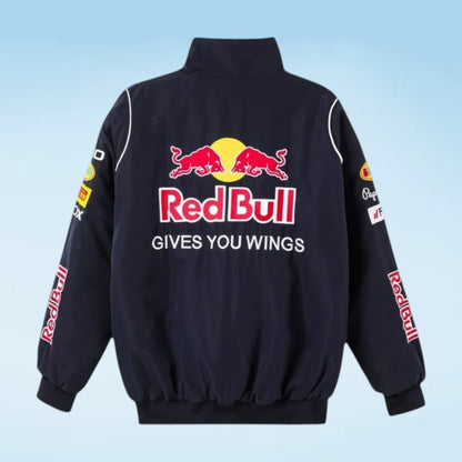 A black Red Bull Racing jacket shown from the back, featuring the iconic red bull logo and 'Red Bull' text in red and yellow, with 'GIVES YOU WINGS' in white below. The jacket has white piping details and Red Bull branding printed down both sleeves.